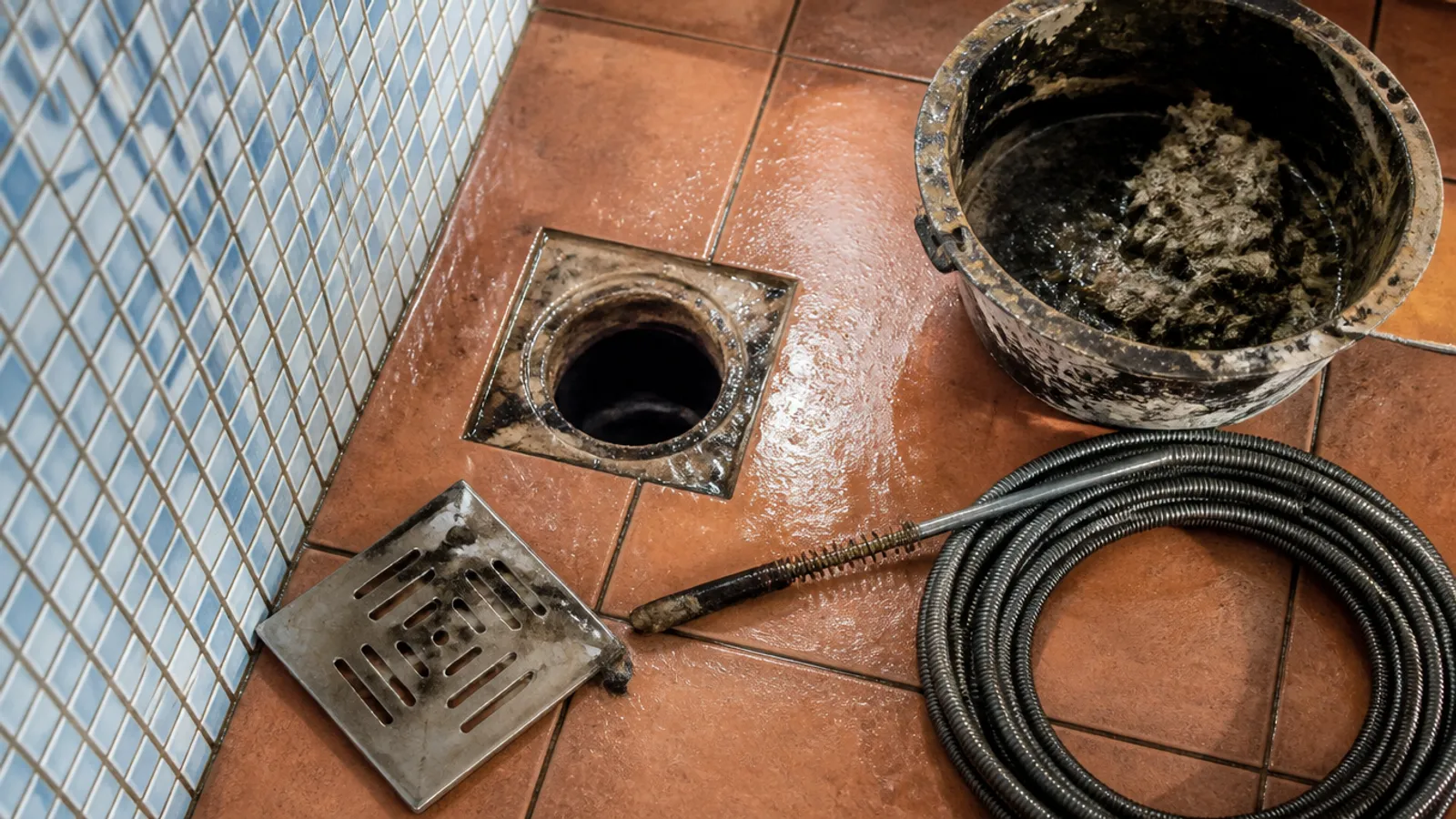 Rejilla de desagüe abierta en un baño con cable de desatasco junto al cubo, trabajo de desatascos en Cabo de Palos